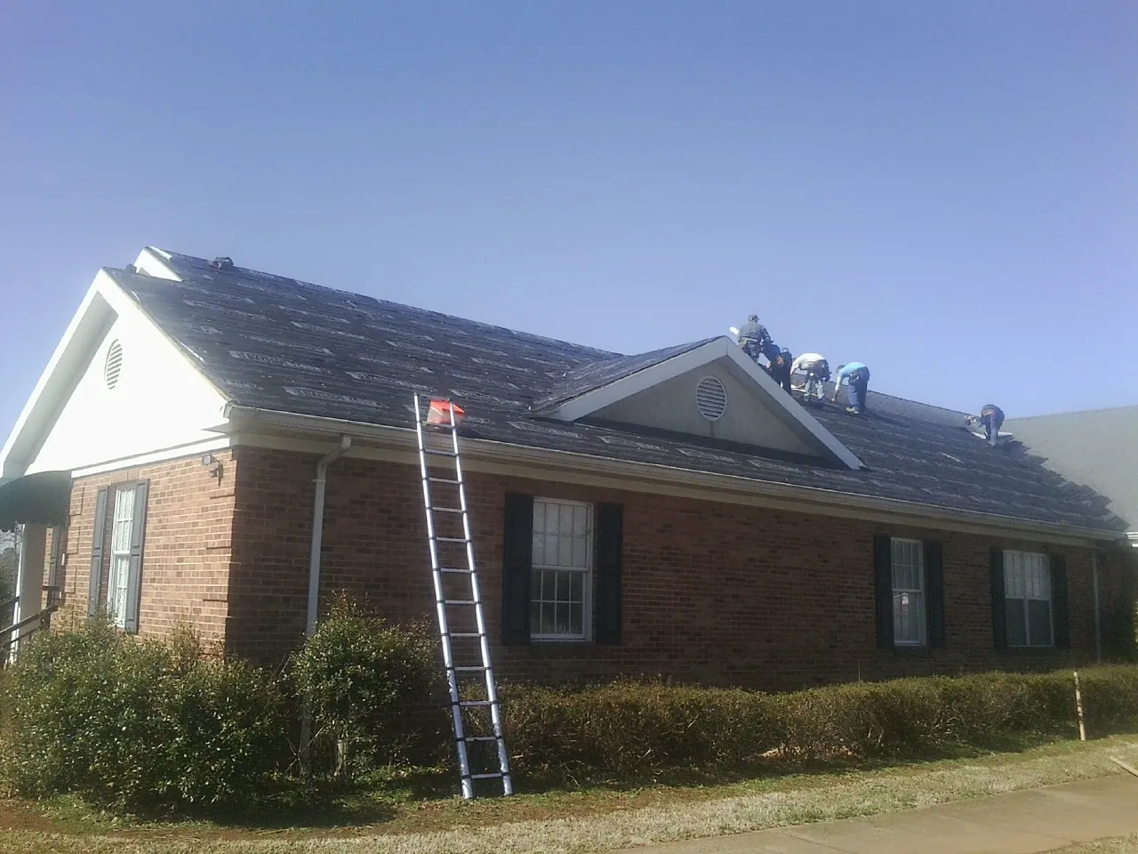 Crew tearing shingles off a brick ranch roof with a ladder set — Metal Roof Repair work by our crew in Marlborough