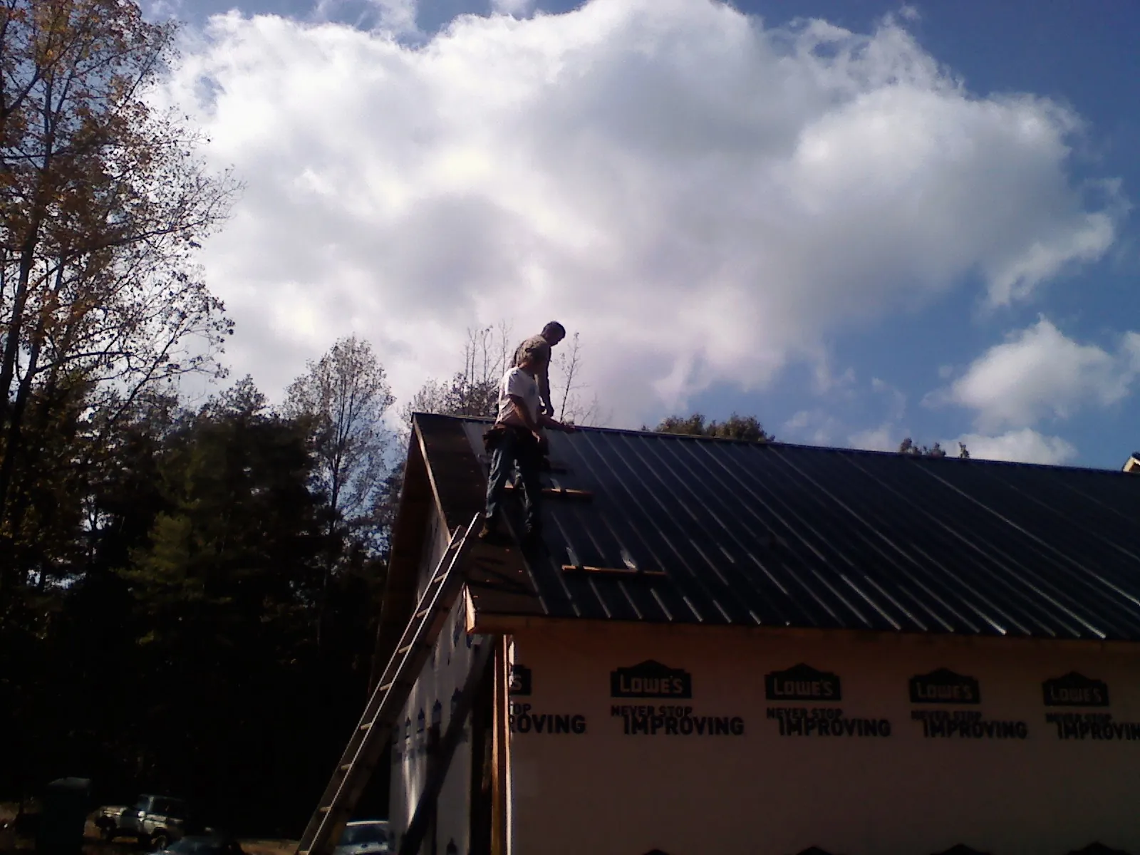 Roofer fastening dark metal panels high against a cloudy sky, from a Roof Inspection job in Marlborough